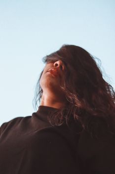 一位长发乌黑的年轻女子，站在户外，背景是清澈的蓝天