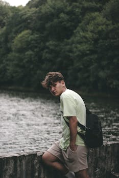 Portrait of a young man standing by a river with lush green trees in Istanbul.