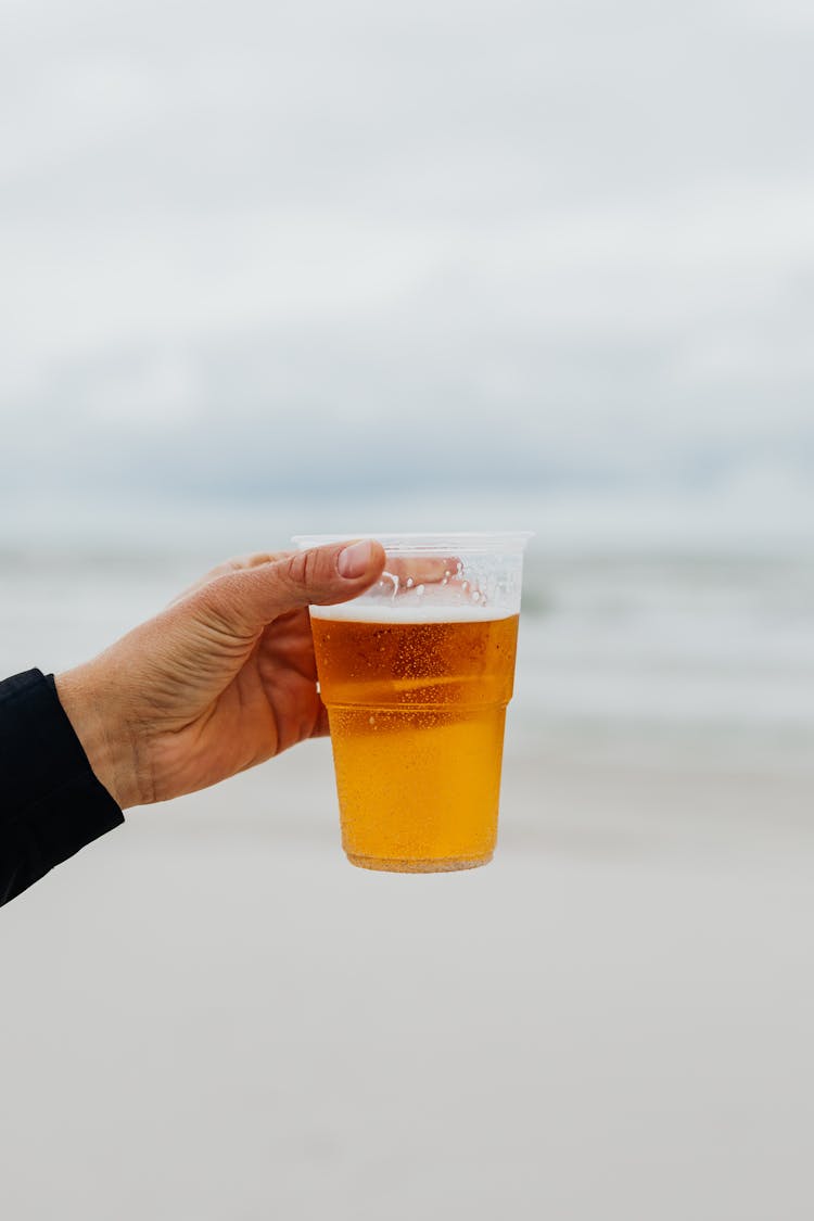 Hand Holding Glass Of Beer On The Beach