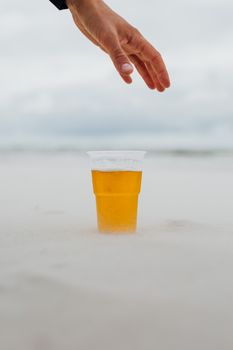 一只手伸向沙滩上的塑料杯，喝了一口清爽的啤酒