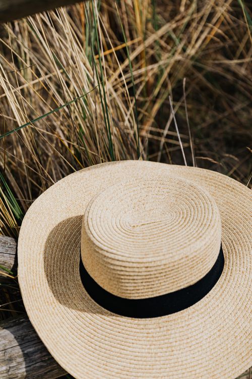Free Stylish straw sun hat with black band on a rustic wooden surface surrounded by dry grass outdoors. Stock Photo