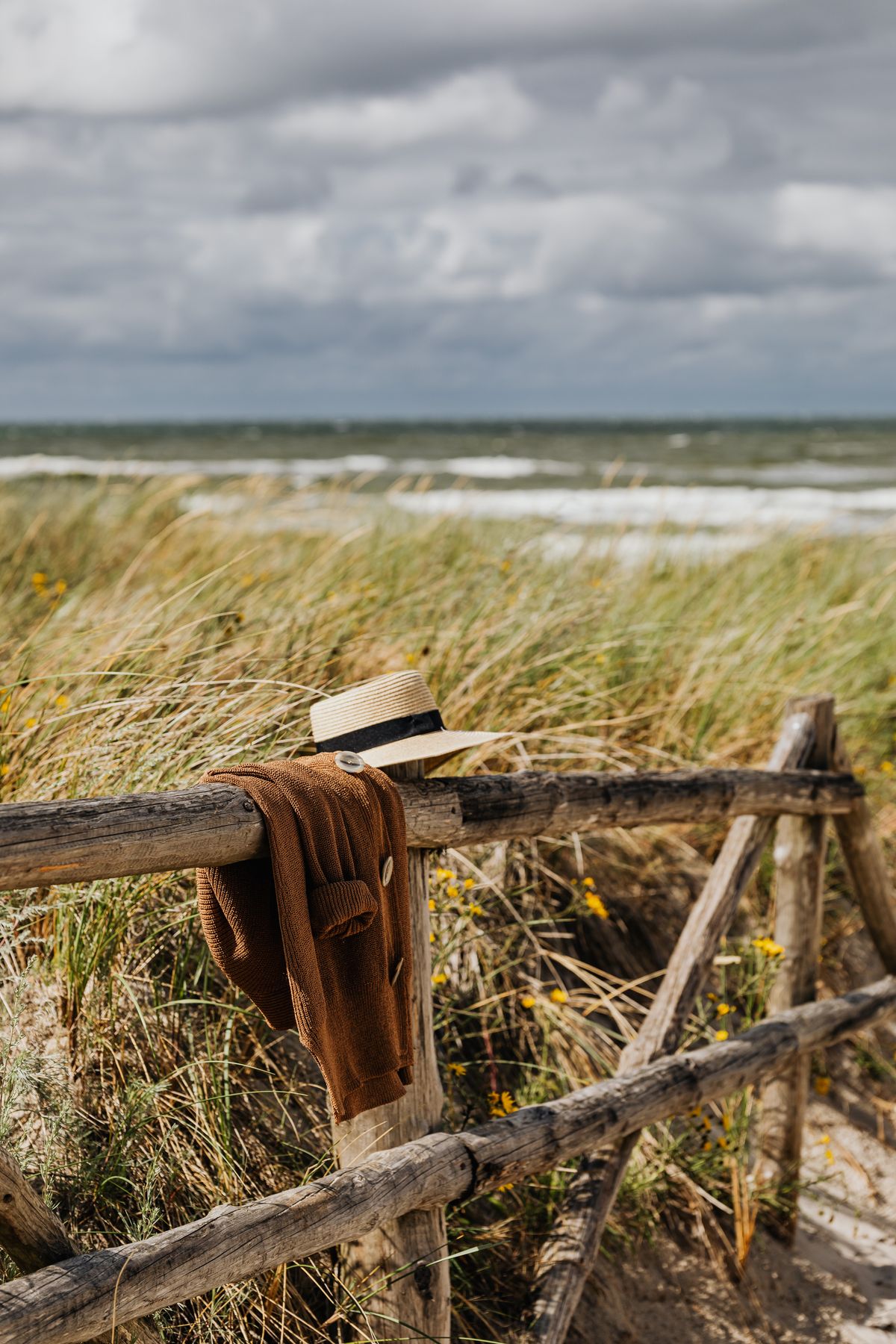 A brown knit sweater and sun hat resting on a wooden fence — the summer knit at rest