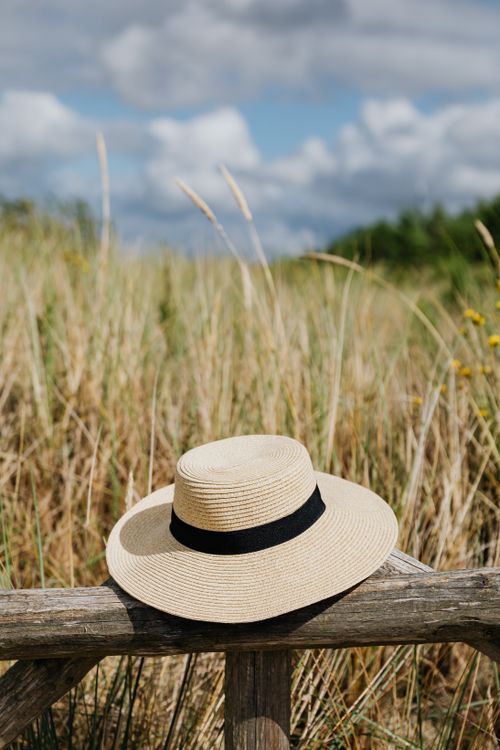 Free A straw summer hat rests on a wooden fence in a grassy field under a blue sky with clouds. Stock Photo