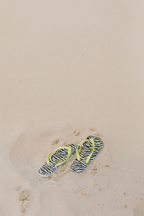 Free Pair of zebra print flip flops resting on a sandy beach, offering a relaxed, summer vibe. Stock Photo