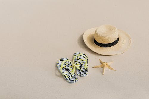 Beach Hat and Flip Flops Slippers Beside a Starfish on a Sandy Shore