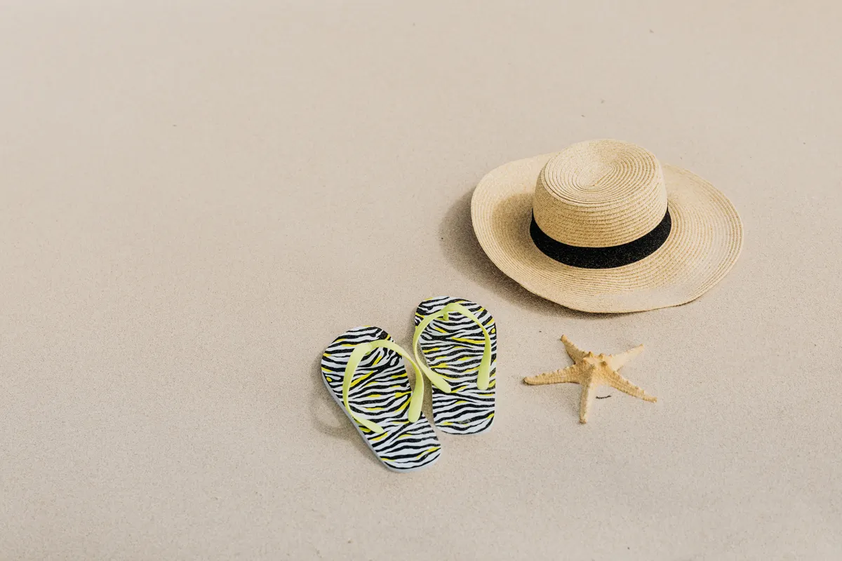 Beach accessories laid out — straw hat, sunglasses, and sandals on the sand