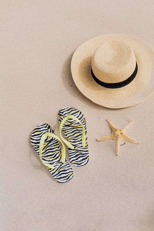 Free A minimalistic summer beach setup featuring a hat, flip flops, and a starfish on sand. Stock Photo