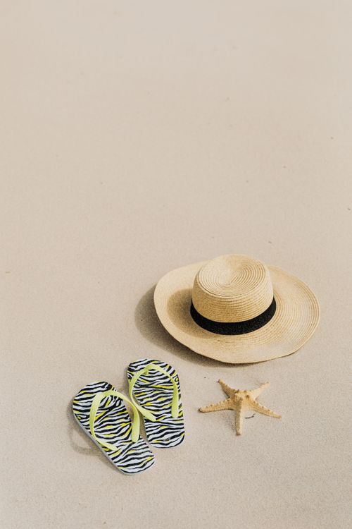 Free A straw hat, flip flops, and starfish on a sunlit sandy beach. Stock Photo