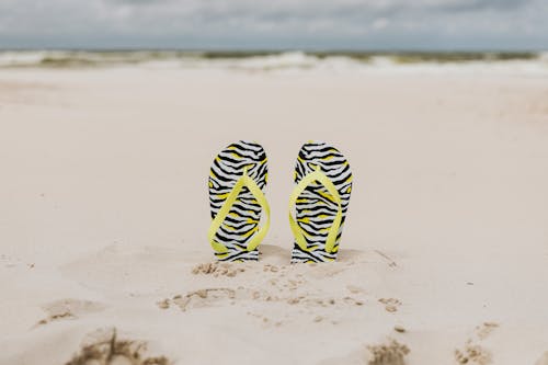 Free Yellow Strapped Slippers Buried on a Sandy Shore Stock Photo