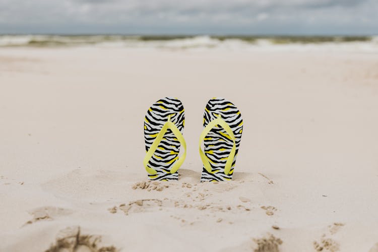 Yellow Strapped Slippers Buried On A Sandy Shore