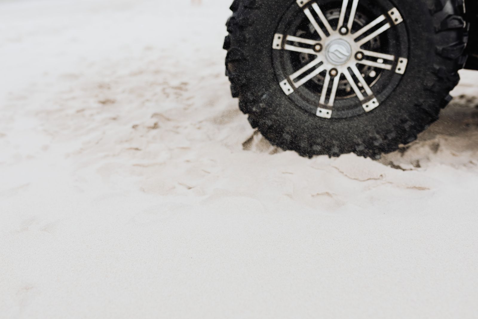 Off-road tire buried and spinning in soft pale sand, the classic no-anchor recovery scenario where a deadman anchor is needed
