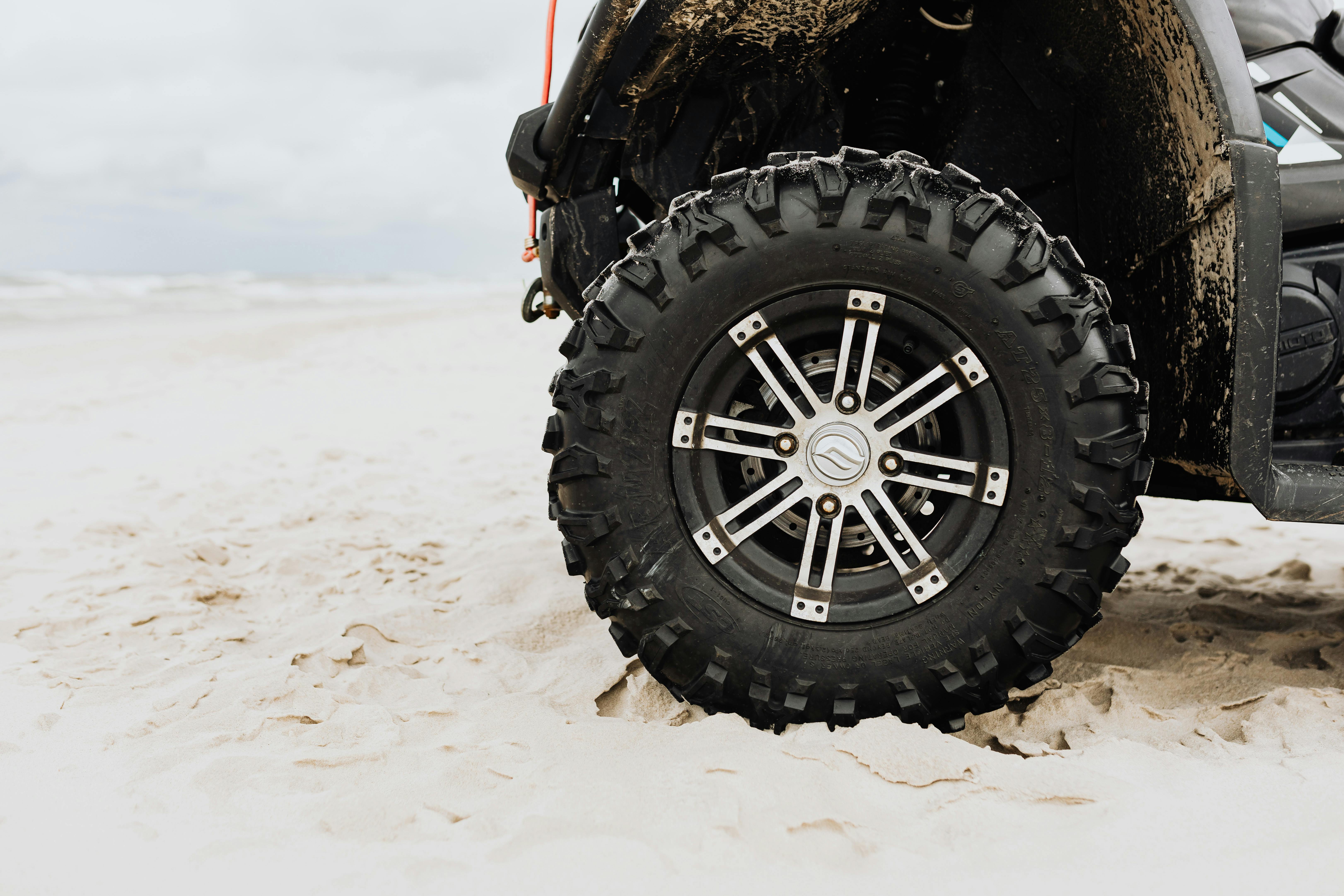 Close-up of an all-terrain vehicle tire on a sandy beach, showcasing rugged design and off-road capabilities.