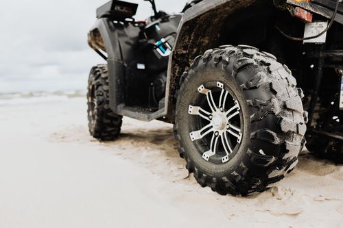 Free Close-up of an ATV tire on a sandy beach, showcasing rugged design and adventure capability. Stock Photo