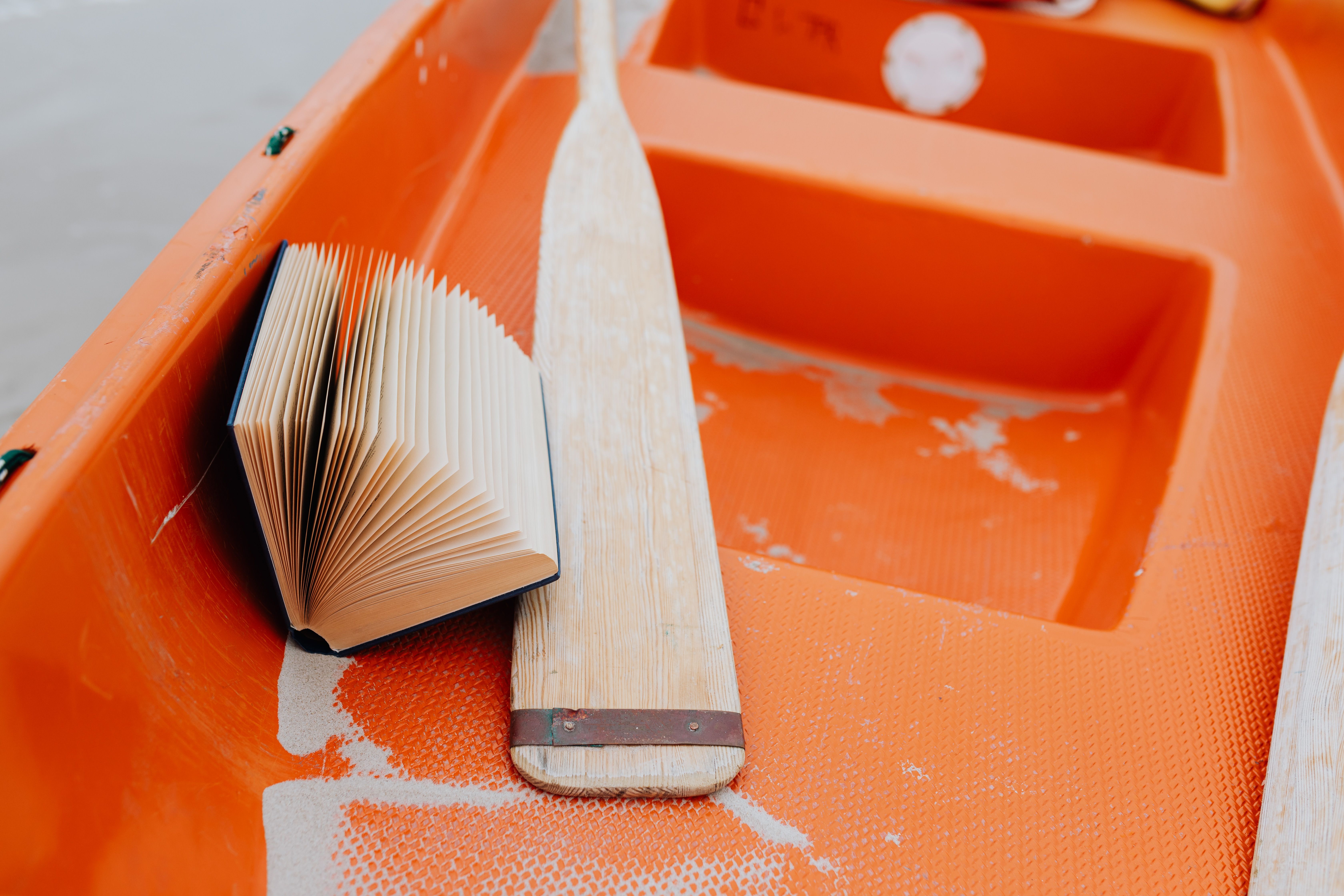 Open book and wooden paddle in an orange boat offer a unique blend of adventure and relaxation.