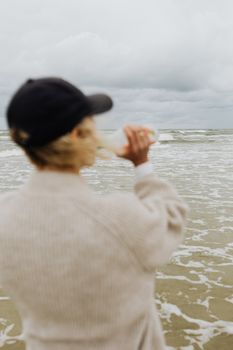 阴天，一个戴着黑帽的女人在海岸线边喝酒，捕捉到一个宁静的时刻