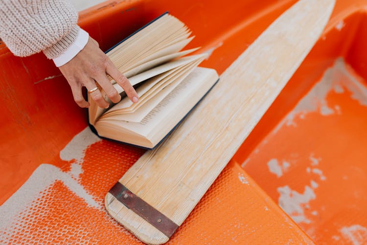 Person Holding A Book Near Wooden Oar