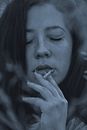 Attractive woman with manicured hand smoking cigarette with closed eyes in blue light