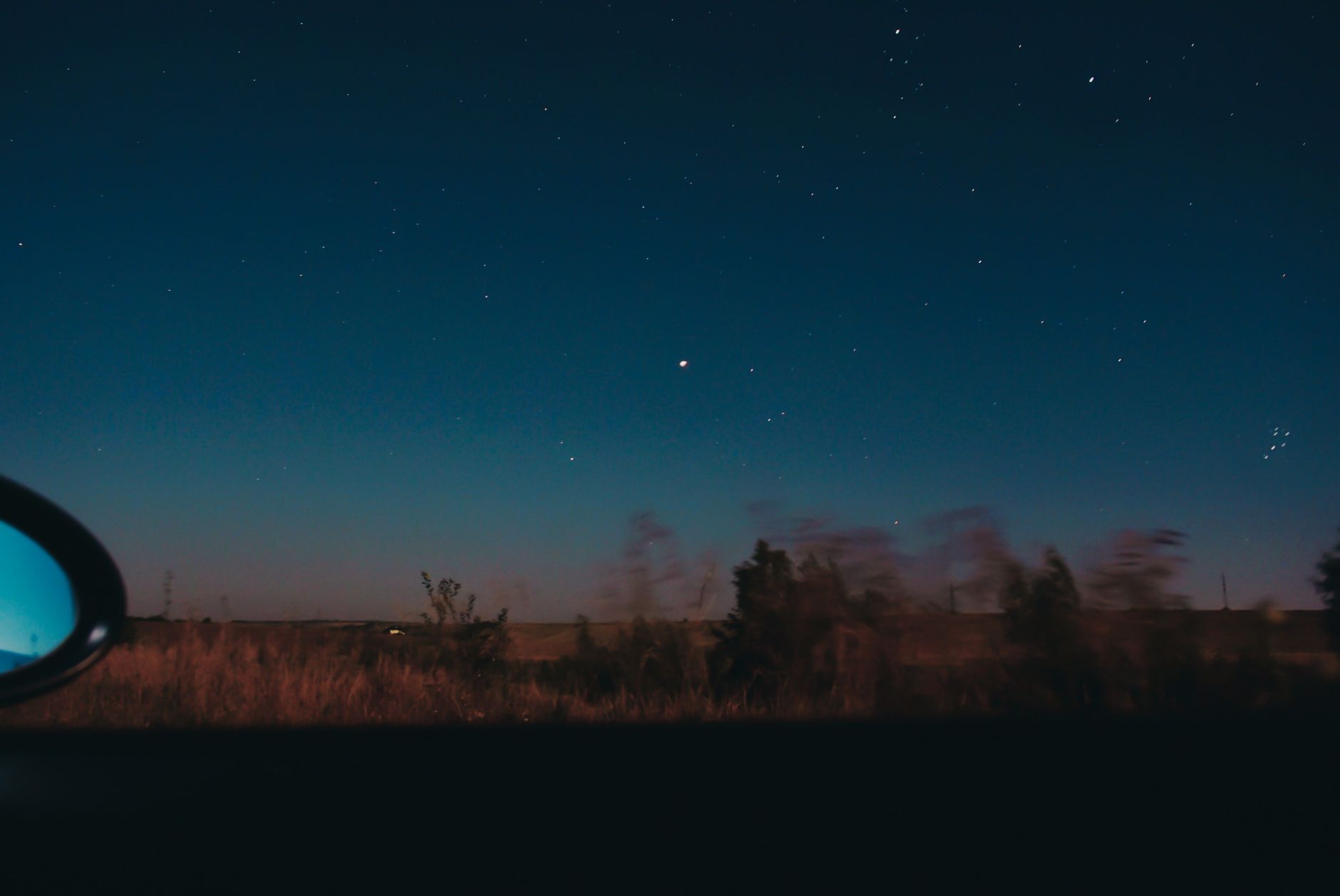 View through moving car window of horizon line with dark star sky and blurred trees