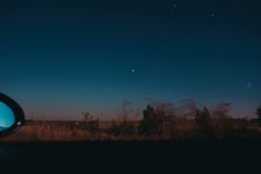 View through moving car window of horizon line with dark star sky and blurred trees