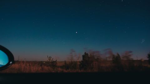 View through moving car window of horizon line with dark star sky and blurred trees