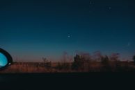 View through moving car window of horizon line with dark star sky and blurred trees