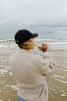 一个戴着黑帽子的女人在多云天空下的海滩上喝酒