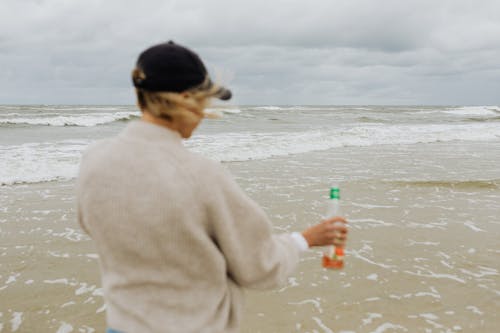 Back View of Person Standing on Beach Shore While Holding Beer