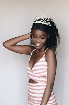 Beautiful African woman with curly hair wearing a crown and striped dress, posing gracefully indoors.