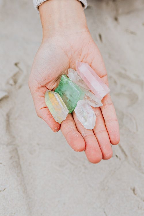 Free Close-up of a person's hand holding colorful gemstones on a sandy beach shoreline. Stock Photo