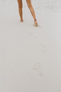 Barefoot person walking on pristine beach sand leaving footprints.