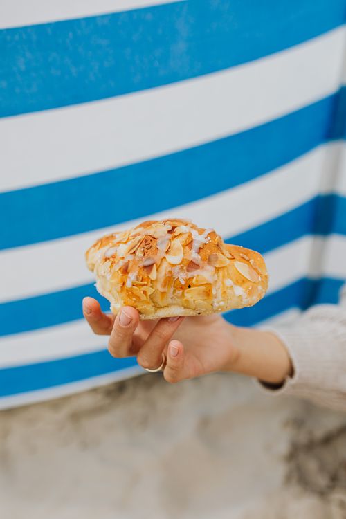 Free Close-up of a hand holding a delicious almond pastry with a blue striped background. Stock Photo