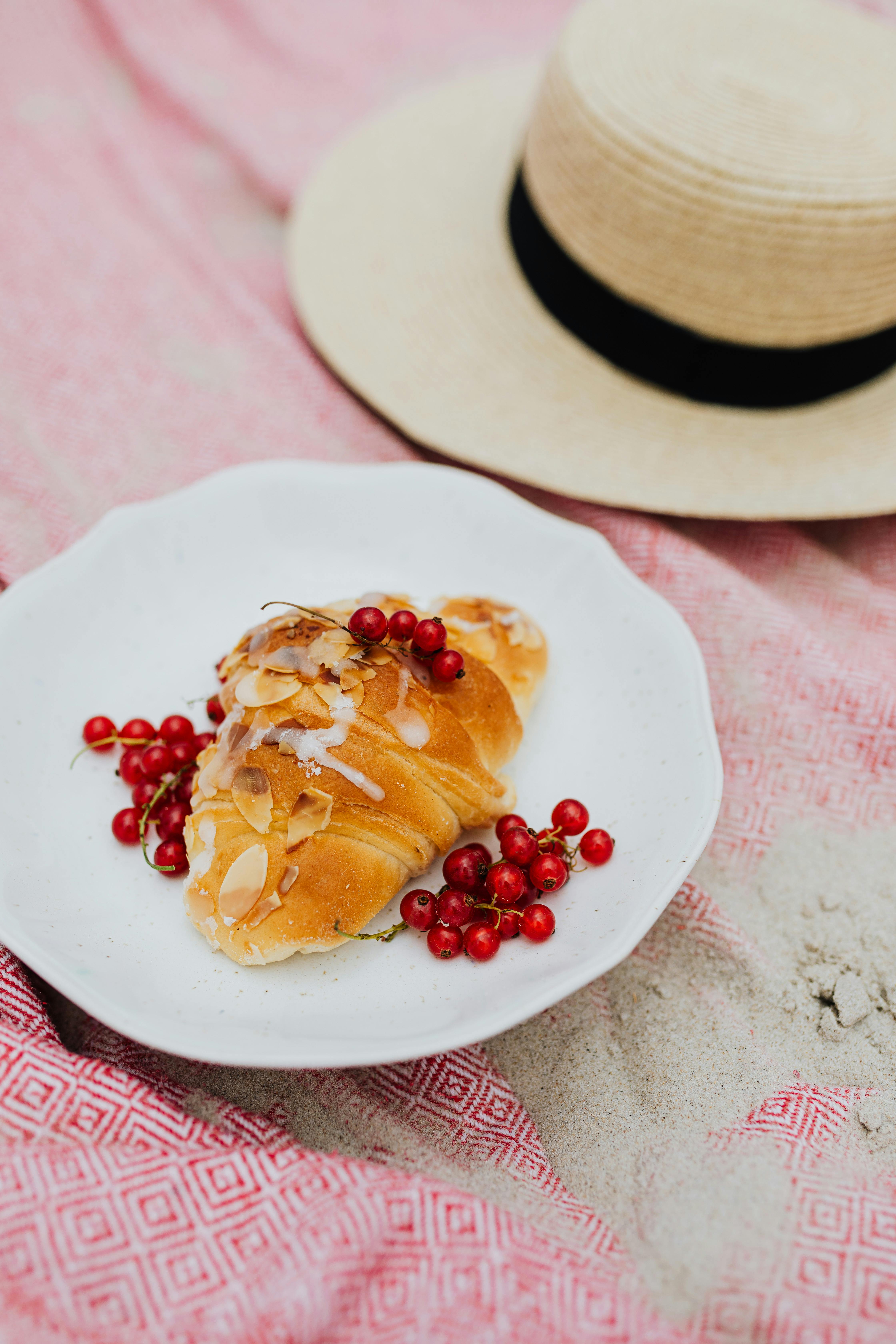 夏季野餐时，新鲜的杏仁羊角面包被放在铺有浆果的盘子里，置于沙滩毯上