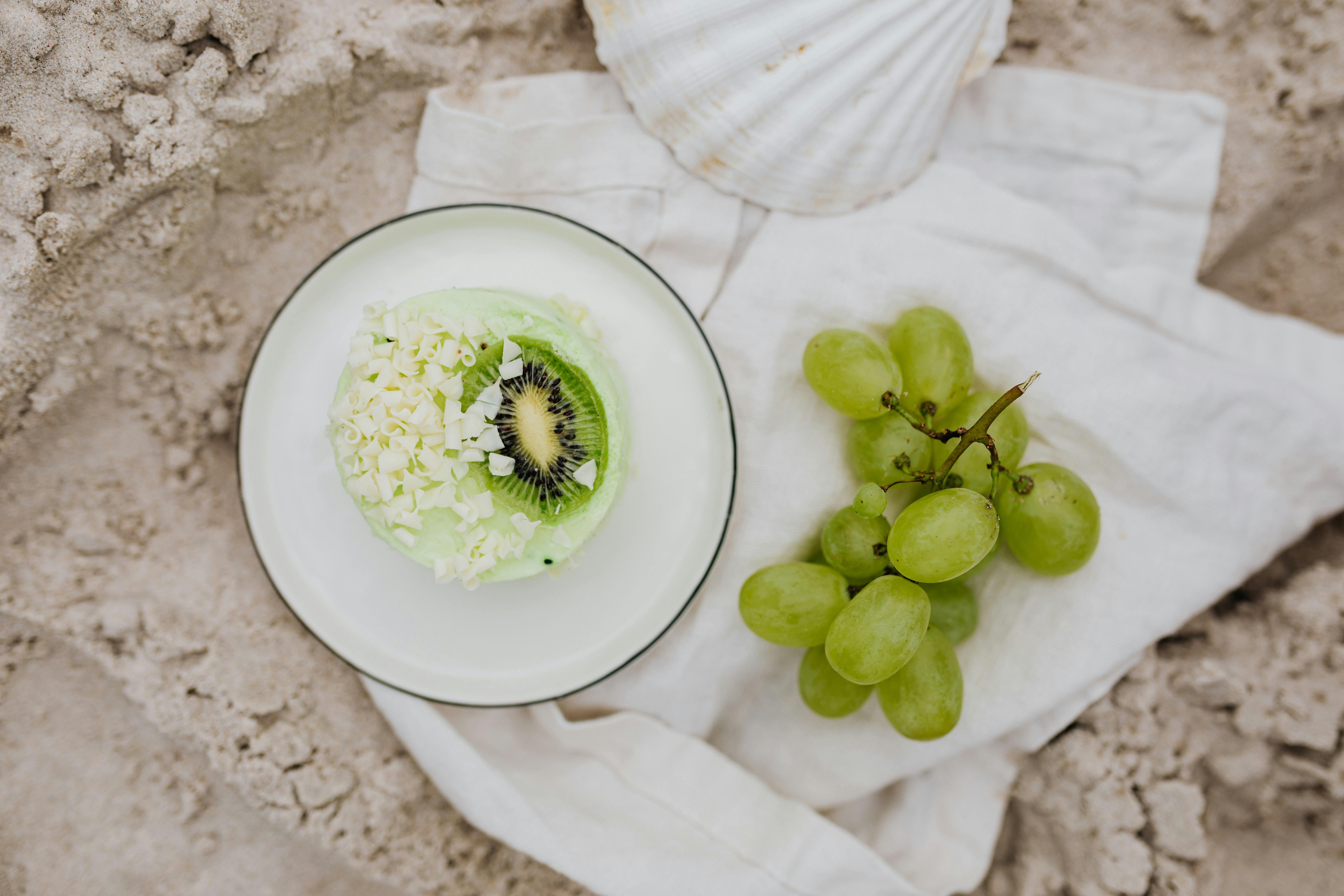 Fresh kiwi and grape dessert styled against a sandy beach backdrop, evoking a sense of summer relaxation.