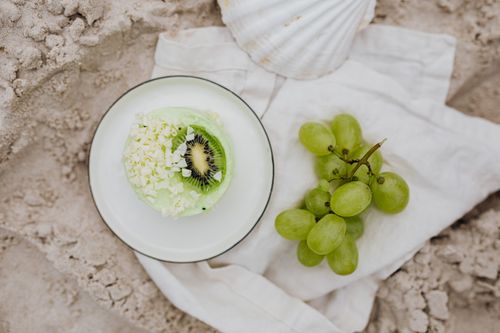 Free Fresh kiwi and grape dessert styled against a sandy beach backdrop, evoking a sense of summer relaxation. Stock Photo