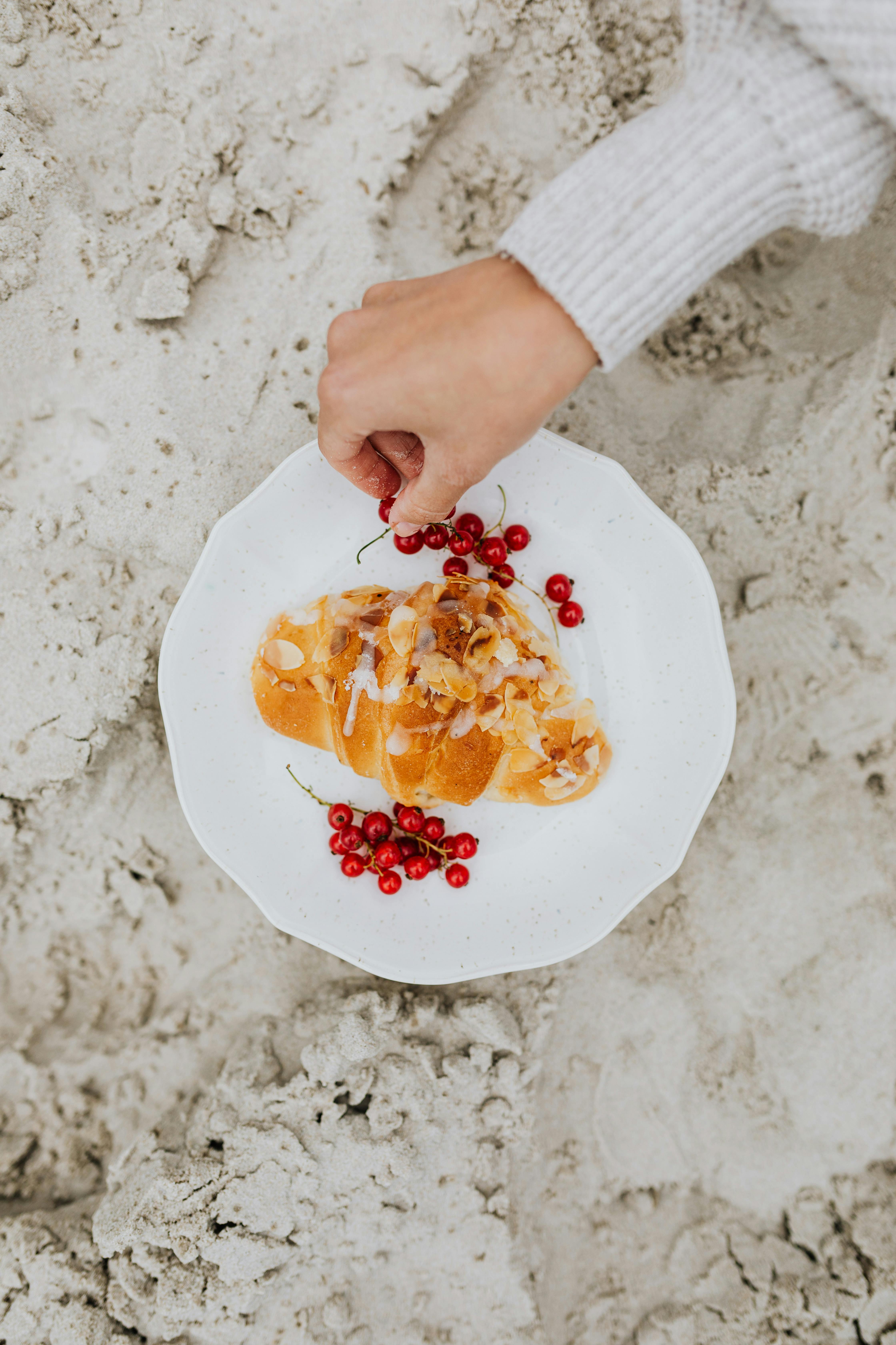 Artistic plating of croissant with red currants on a sandy beach, showcasing unique food styling.