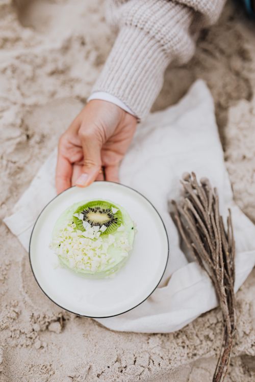 Free A close-up of a kiwi-topped dessert held above sand, showcasing a tropical treat. Stock Photo