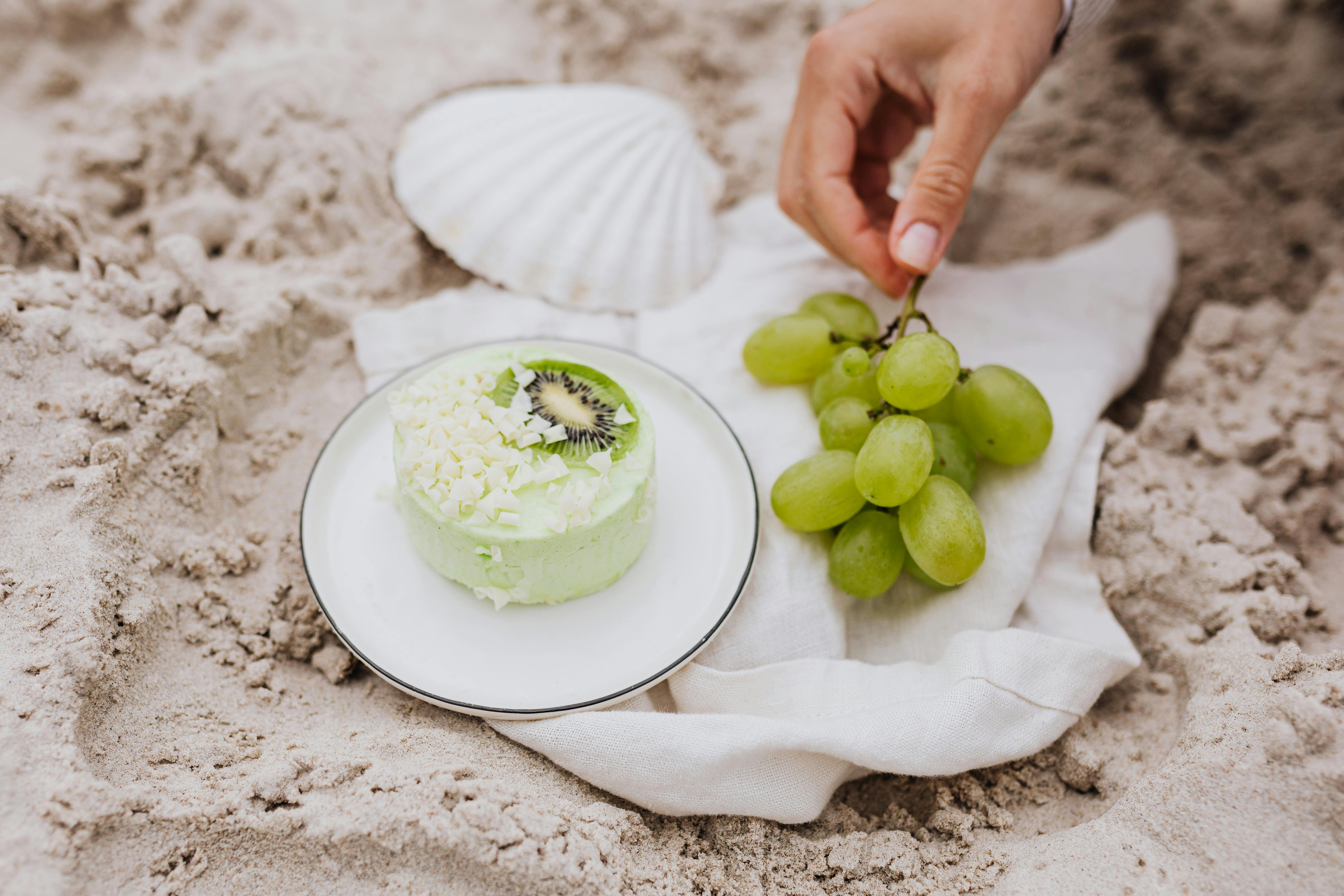 沙滩上特写的绿色甜点与葡萄和贝壳