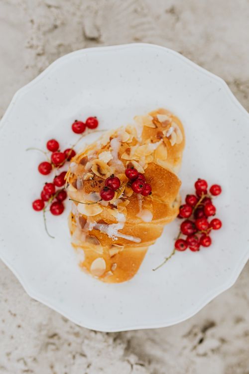 Free A delectable croissant topped with sliced almonds and fresh red currants on a ceramic plate. Stock Photo