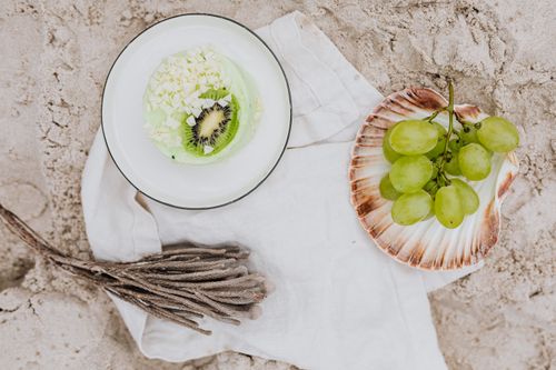 Free A top-down view of a kiwi and grape dessert arrangement on sandy beach backdrop. Stock Photo