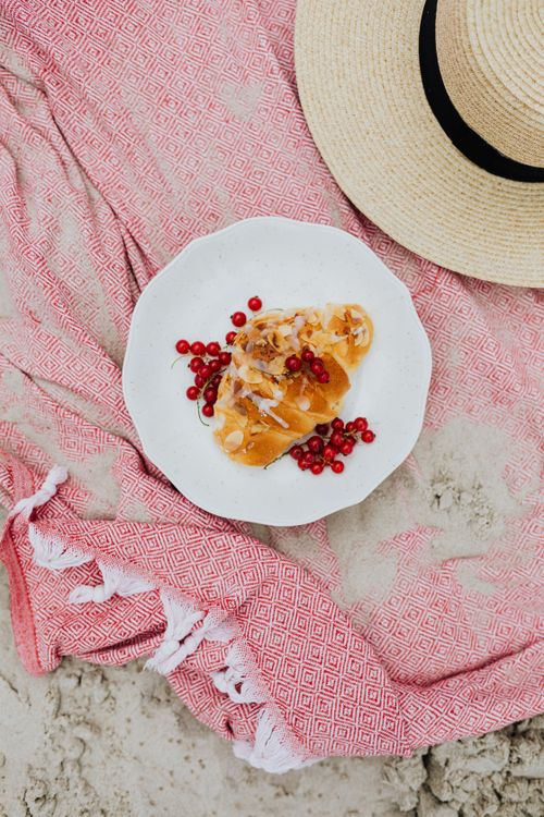 Free Tasty croissant with red currants on beach sand with a straw hat nearby. Stock Photo