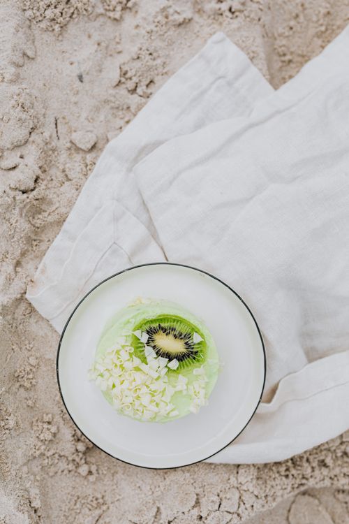 Free Fresh kiwi dessert on sandy beach with white chocolate flakes, top view. Stock Photo