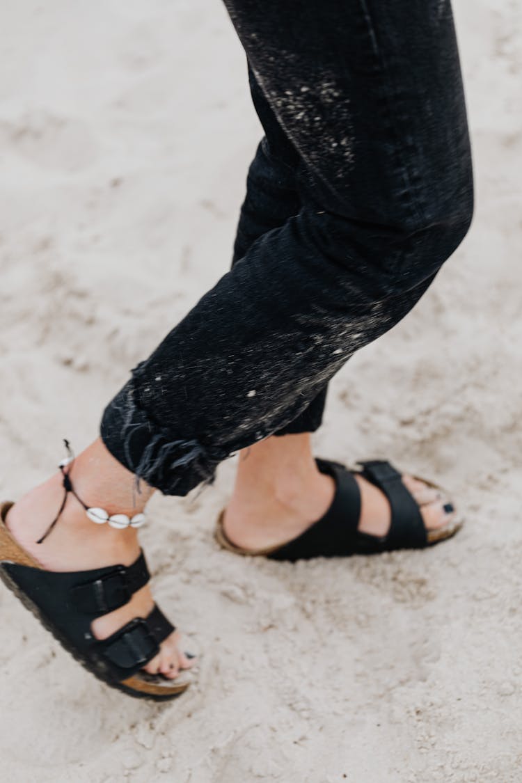 Person In Black Pants And Black Sandals Walking On The Sand