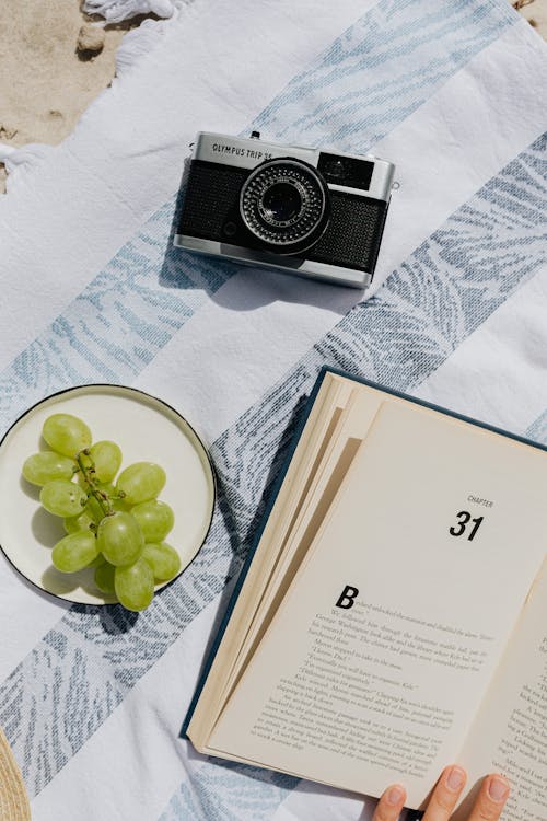Green Grapes on a Saucer Beside an Analog Camera and Open Book