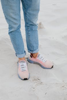 Stylish sneakers paired with rolled-up jeans walking on sandy beach.