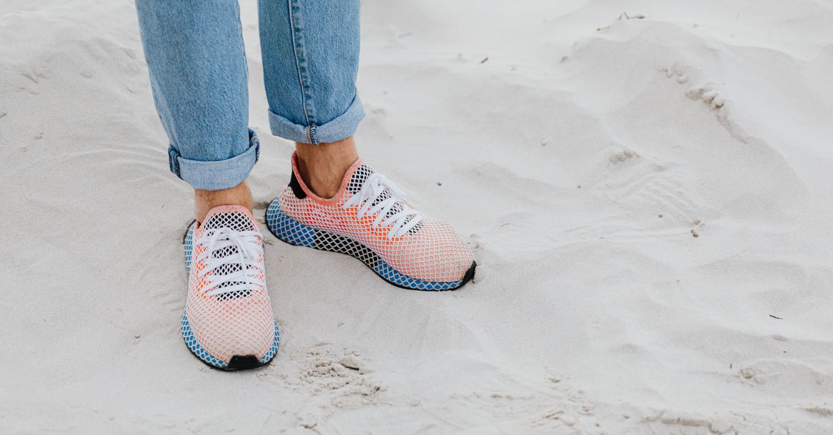 A close-up of a person's legs wearing sneakers walking on a sandy beach.