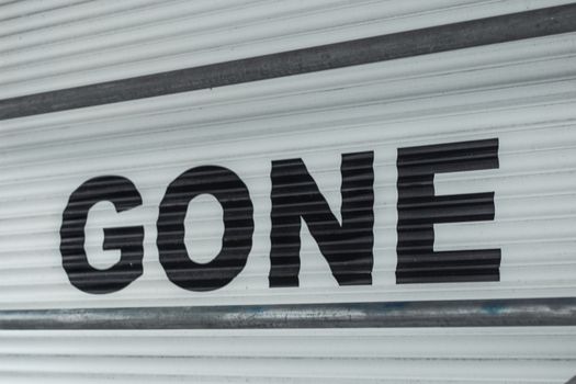Close-up of a corrugated steel shutter with bold black 'Gone' text, providing a minimalist industrial vibe.