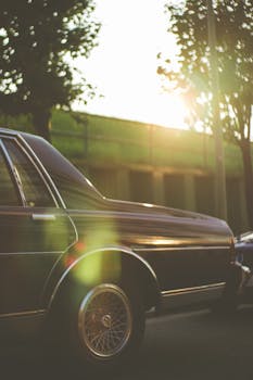 Elegant black vintage car cruising on a sunlit road with lush greenery in the background.