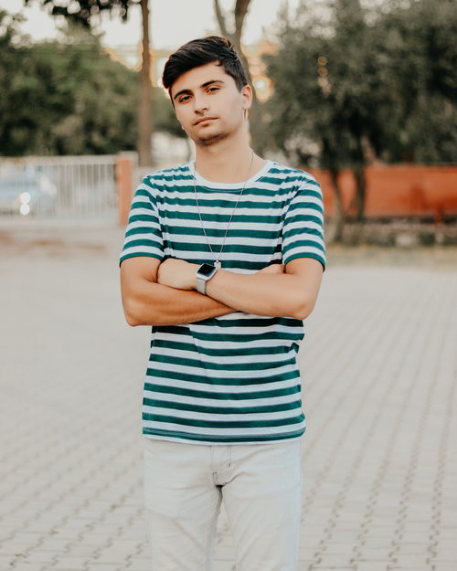 Free Young man posing with arms crossed in a striped shirt outdoors. Casual and confident demeanor. Stock Photo