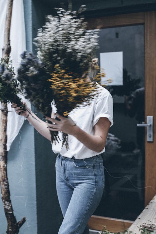Crop unrecognizable female in casual wear walking with bouquet of fresh flowers near florist shop