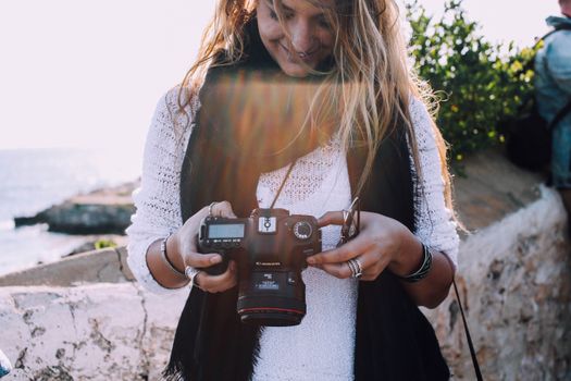 Content young female traveler checking pictures on photo camera while spending holidays at seaside